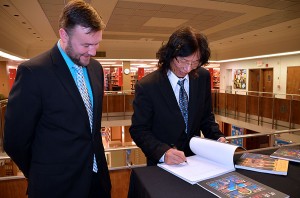 Rev. Benjamin Haupt, director of library services, stands by as He Qi signs a book of his art to donate to the library.
